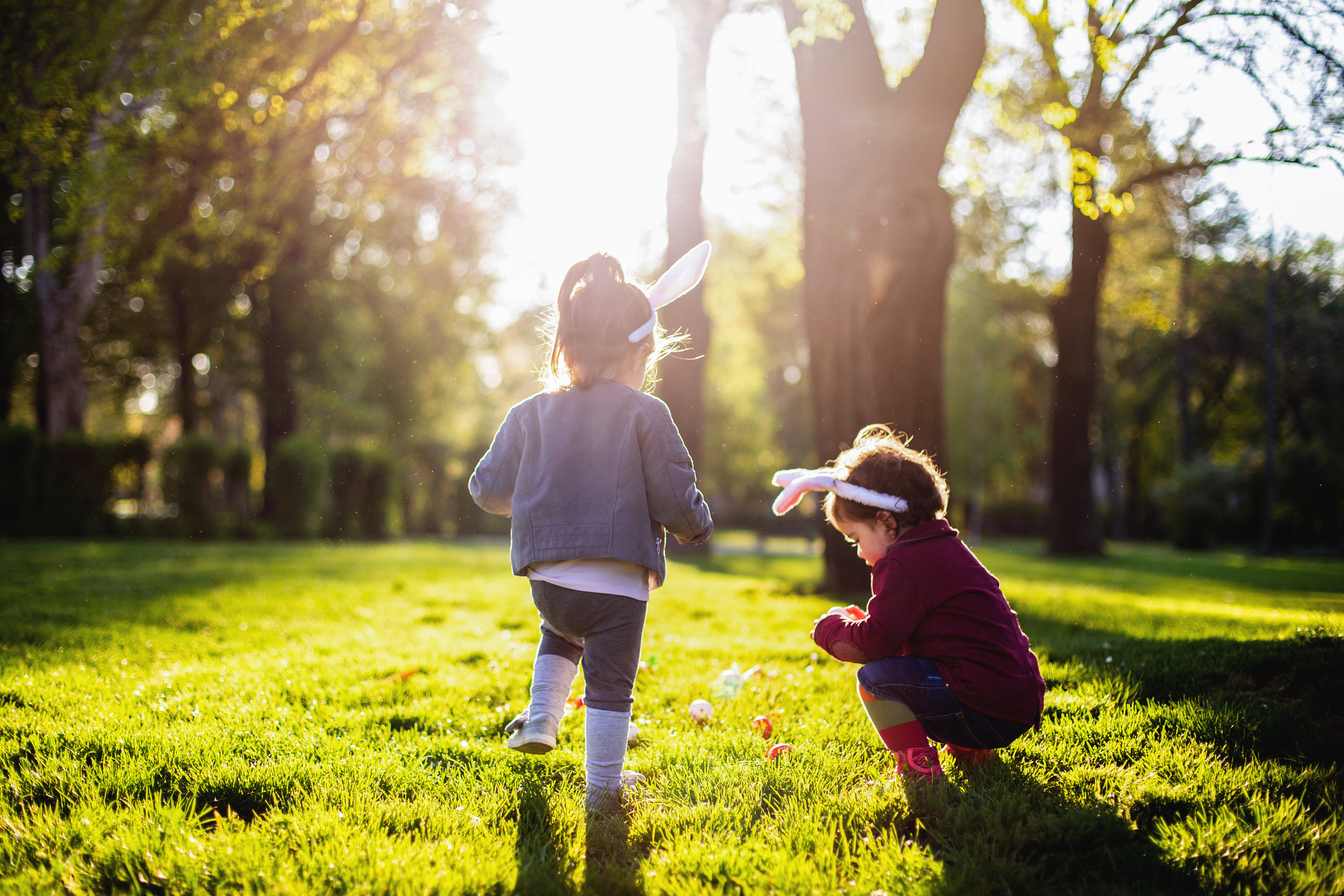 Two children searching for Easter eggs in grass wearing bunny ears